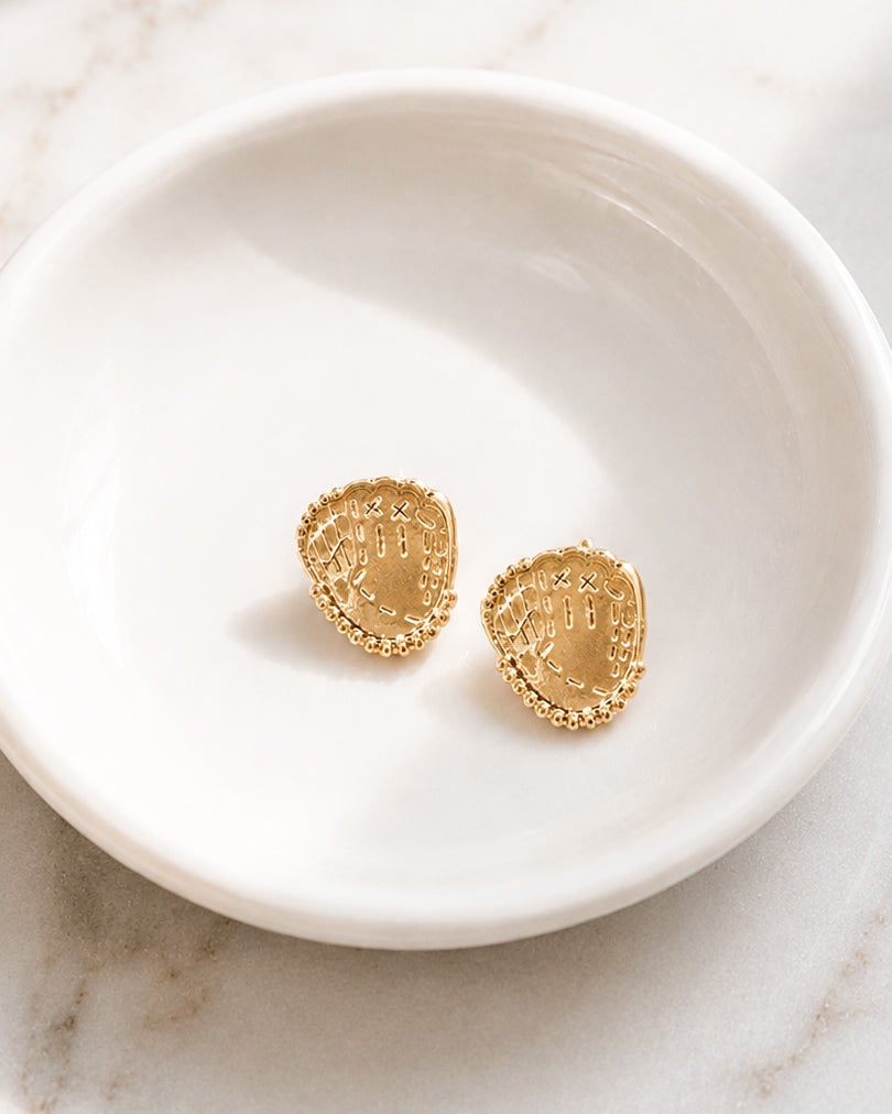 Shiny gold baseball glove stud earrings displayed on a white ceramic jewelry dish.