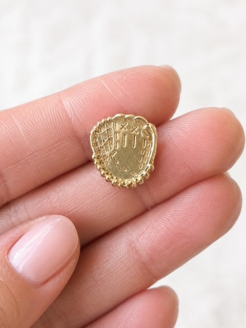 Close-up of a shiny gold baseball glove stud earring held between fingers.