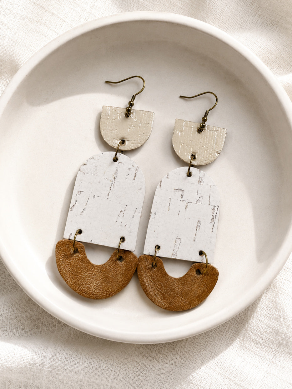Golden Birch cork and leather statement earrings displayed in a white ceramic dish.