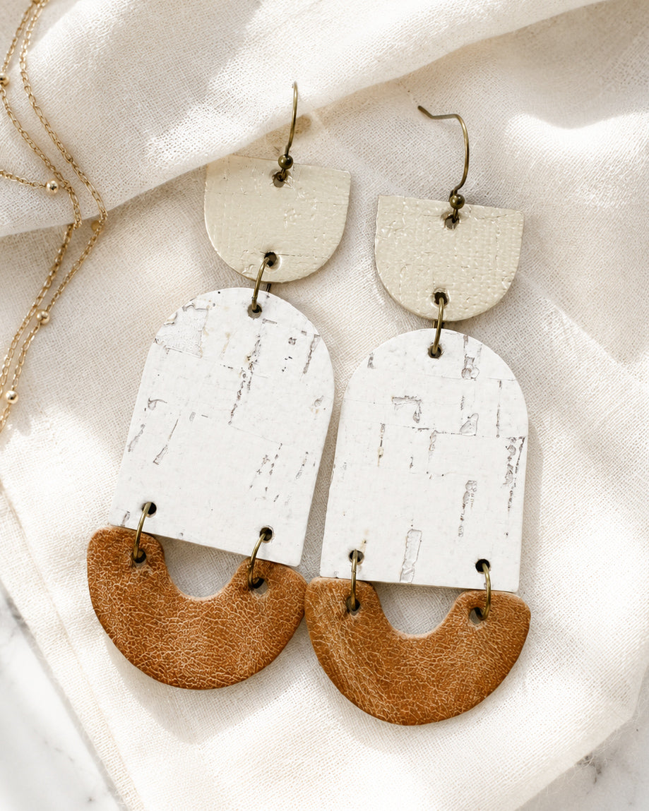 Golden Birch handmade cork and leather statement earrings with platinum, ivory, and camel layers on soft ivory linen.