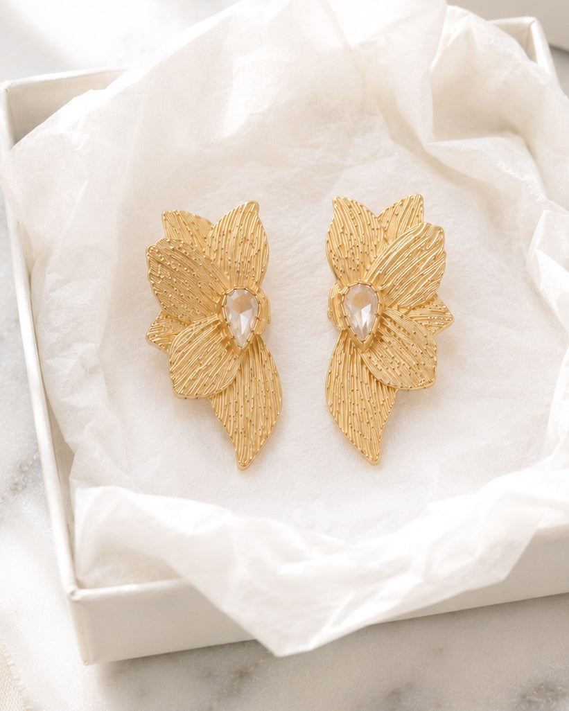 Golden Magnolia Studs gold floral statement earrings displayed inside an open cream velvet jewelry box on white marble.