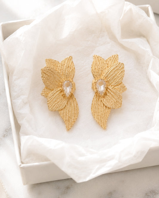 Golden Magnolia Studs gold floral statement earrings displayed inside an open cream velvet jewelry box on white marble.