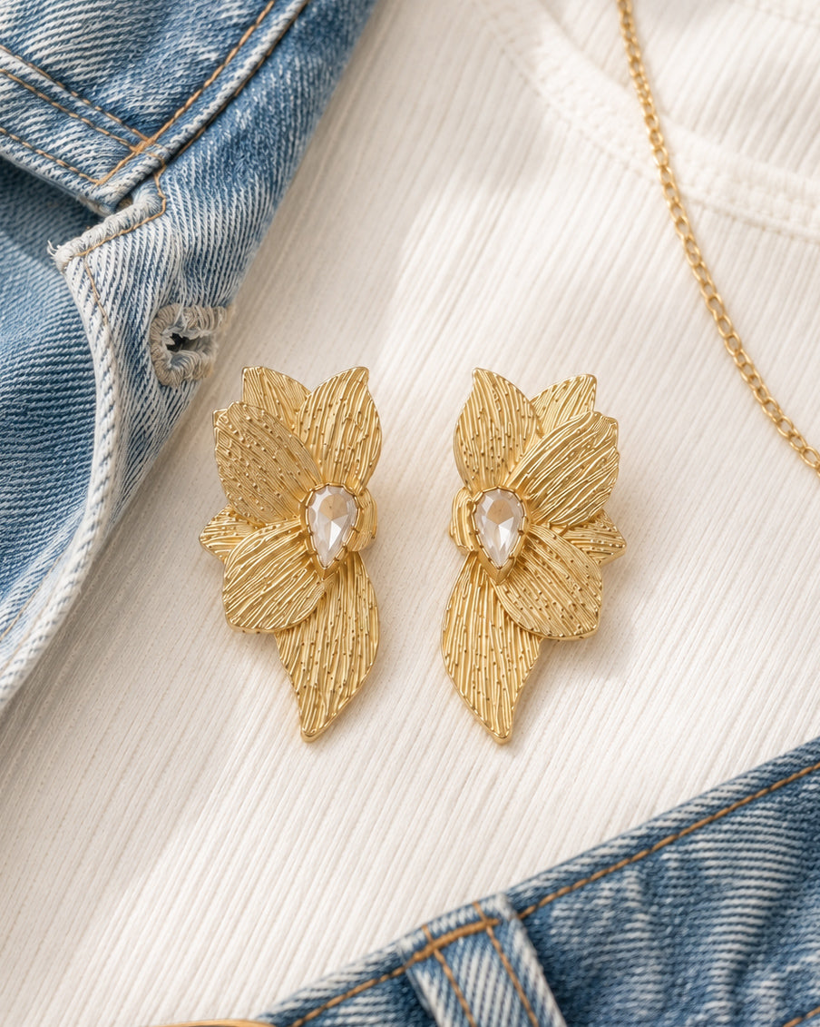 Gold floral statement earrings styled with an ivory sweater, denim, blush quilted handbag, and nude ballet flats.
