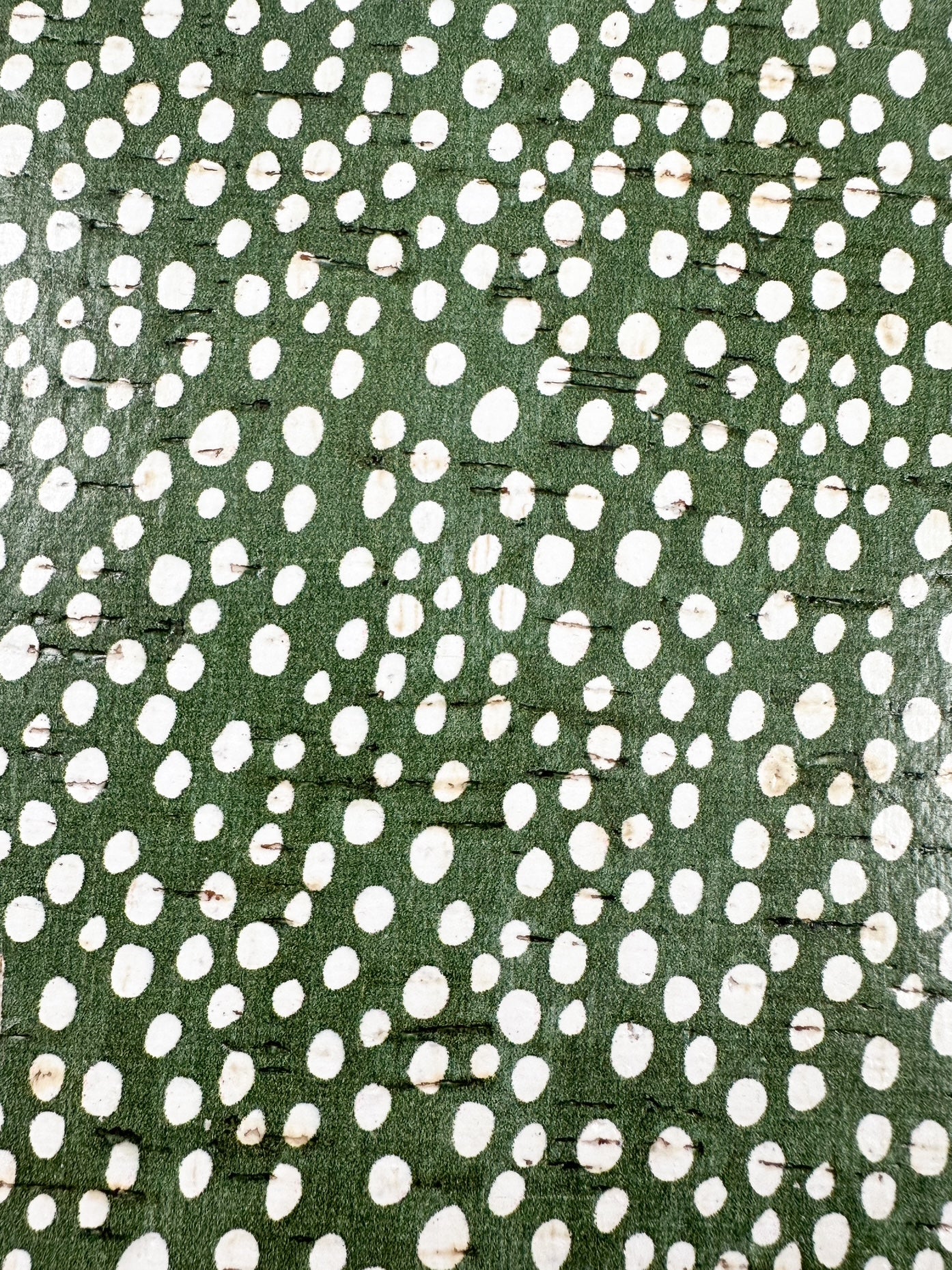 Close-up of green cork leather with natural bark texture and scattered white polka dots, used in handmade teardrop earrings.