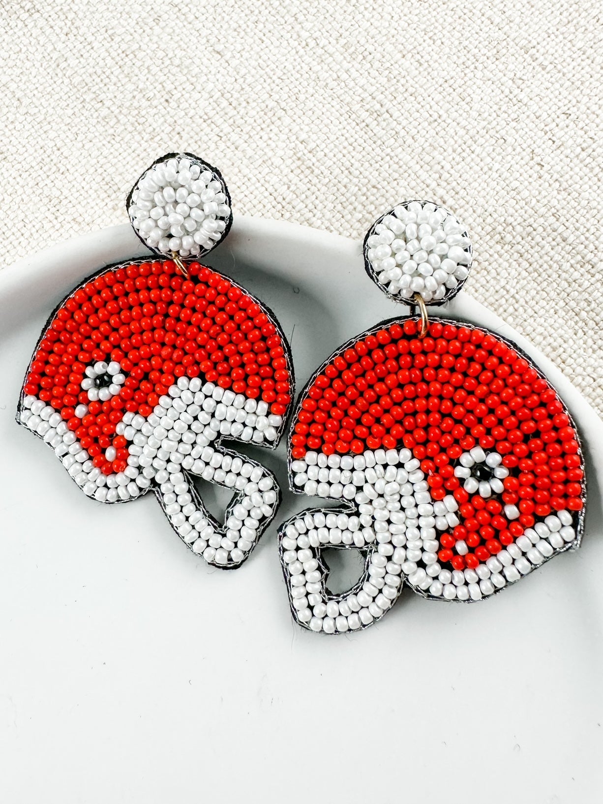 Close-up of red football helmet seed bead earrings showing detailed beadwork, felt backing, and gold-tone connectors.