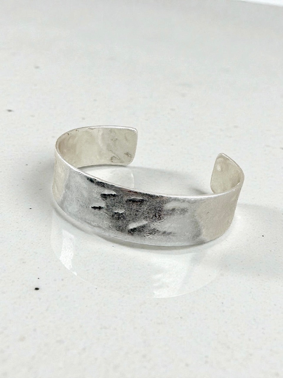 Wide hammered silver-tone open cuff bracelet with distressed antique finish displayed on white background.