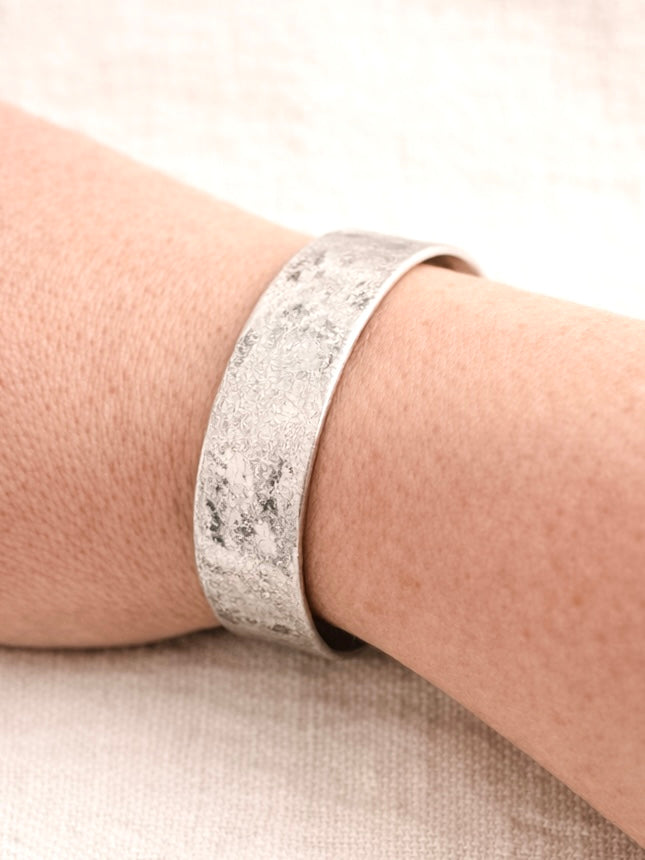 Hammered worn silver-tone cuff bracelet with distressed antique texture shown worn on wrist.