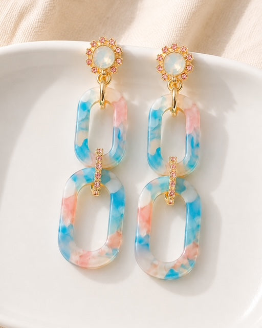 Hampton Drop Earrings with blue and pink watercolor-inspired marbled links, iridescent opal-like studs, and gold accents displayed on a white dish.