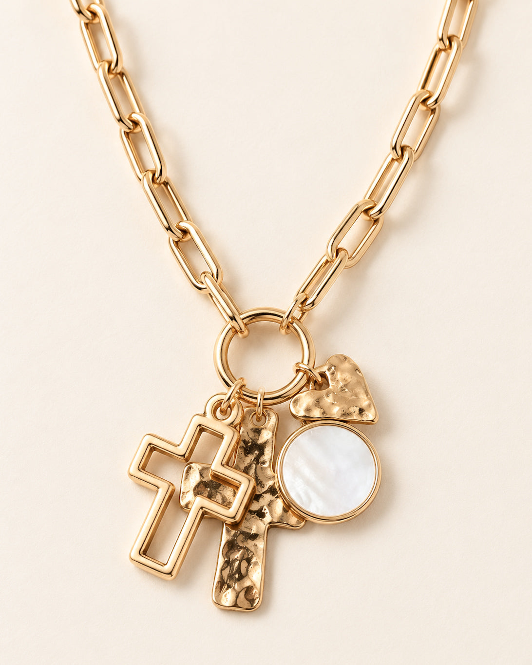 Close-up of Heart & Soul Necklace featuring two gold cross charms, a hammered gold heart, and a round pearly charm on a gold paperclip chain.