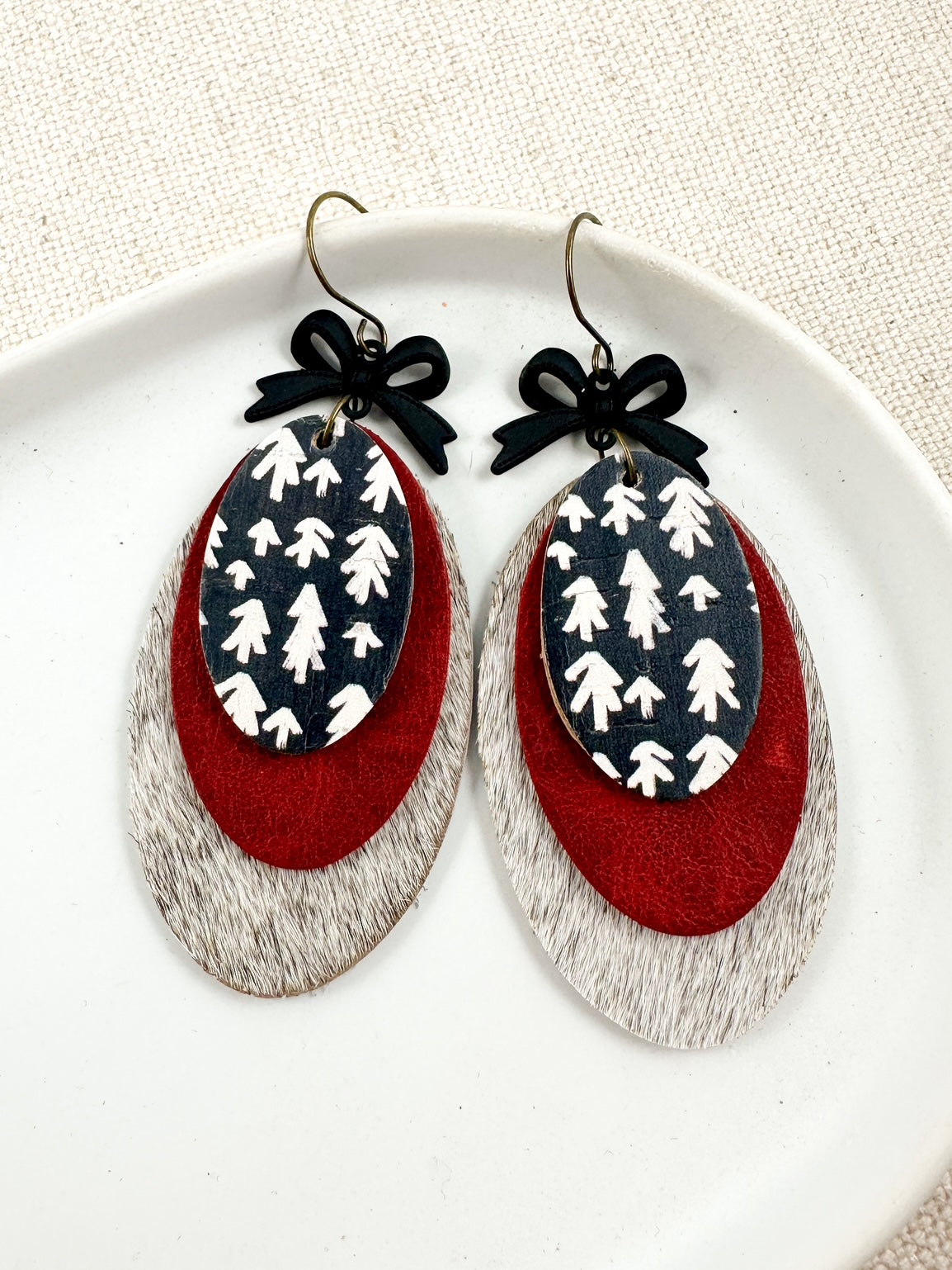 Heirloom Pines Earrings displayed on a white plate, showing layered red leather, black and white tree print, and black bow accents.