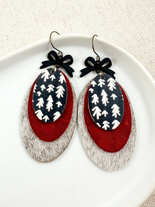Heirloom Pines Earrings displayed on a white plate, showing layered red leather, black and white tree print, and black bow accents.