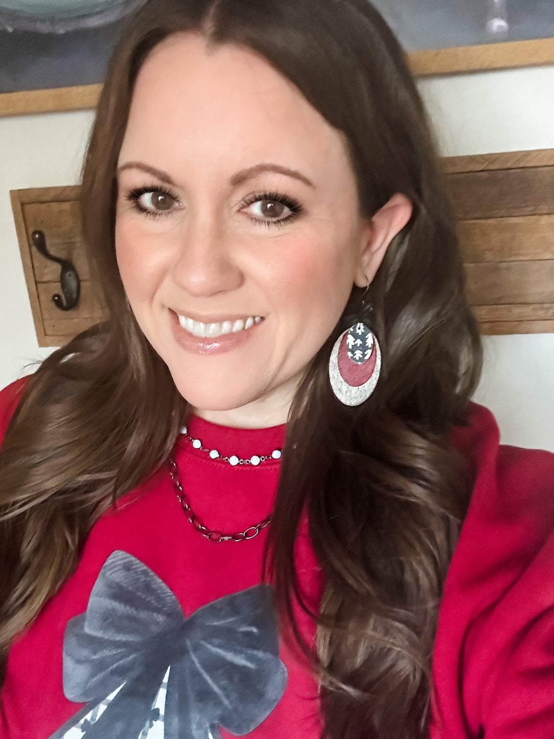 Model smiling while wearing the Heirloom Pines Earrings and red Velvet Pines Sweatshirt with plaid tree design.