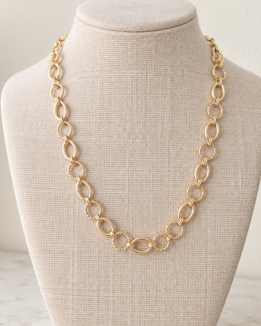 In the Loop gold link necklace displayed on a neutral linen jewelry bust