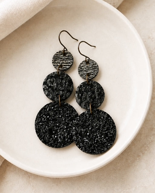 Handmade black circle earrings styled on a white dish with leopard print, black glitter, and metallic details