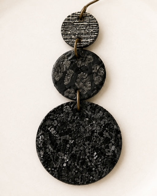 Close-up of black circle earrings showing glitter, leopard print, and metallic silver and gold threads