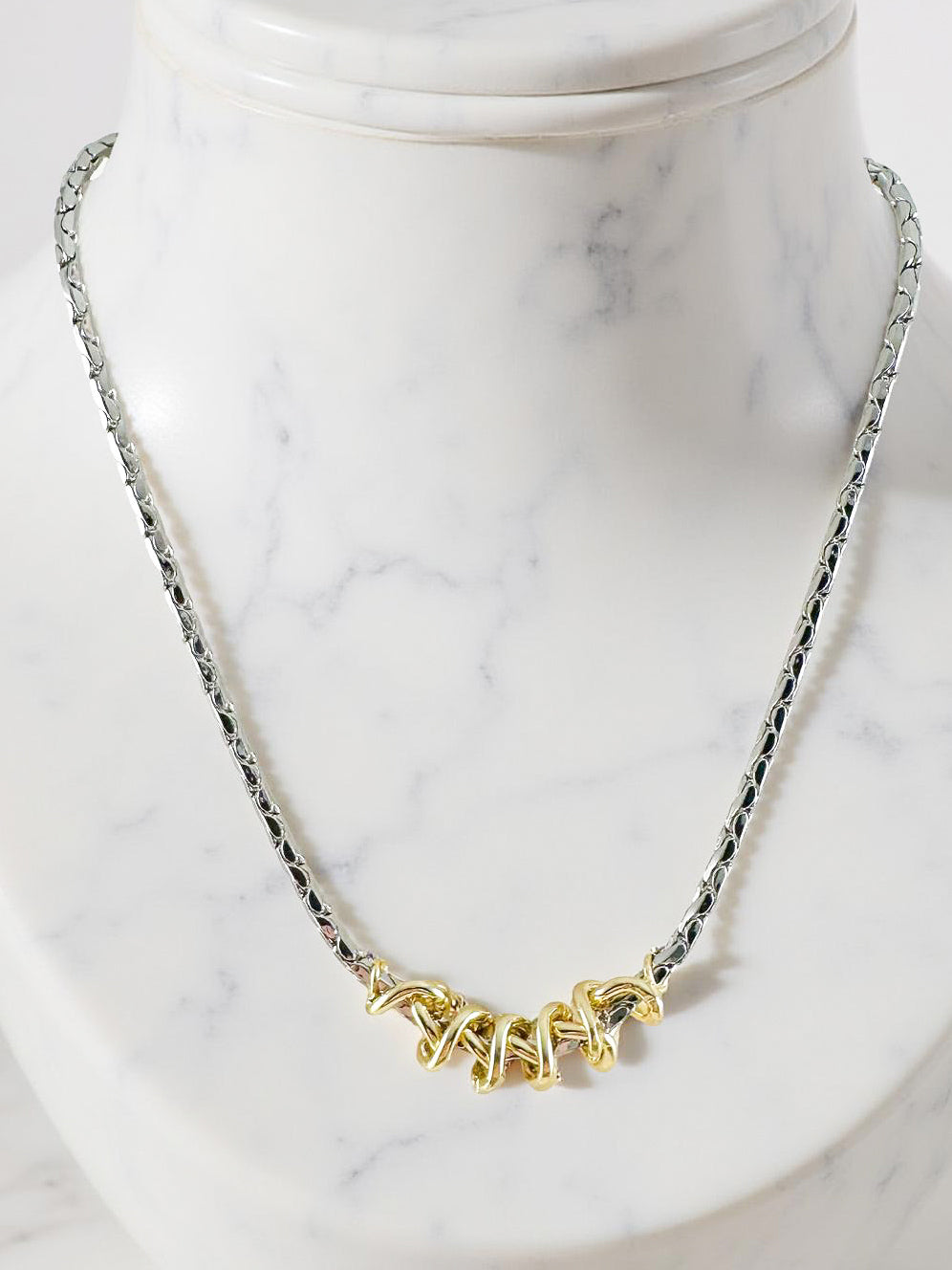 mixed metal necklace with silver chain and gold knot style center shown on marble bust
