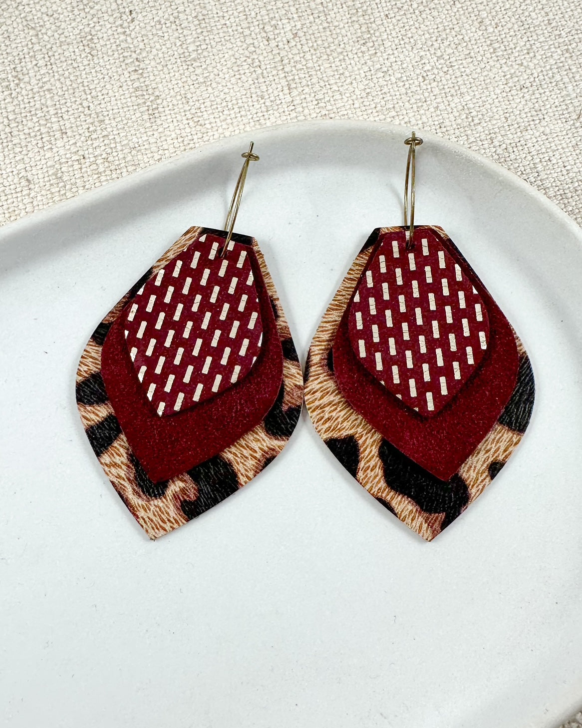 Layered leather hoop earrings with maroon suede, maroon patterned leather, and leopard print leather on antique bronze hoops, arranged on a neutral plate
