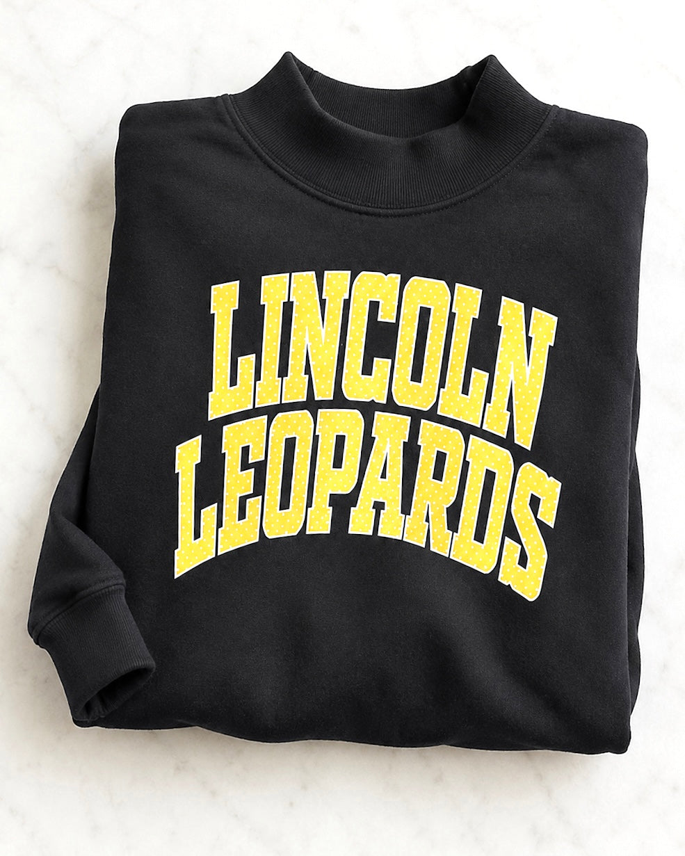 Folded black Leopard Legacy Mockneck with yellow polka-dot Lincoln Leopards lettering
