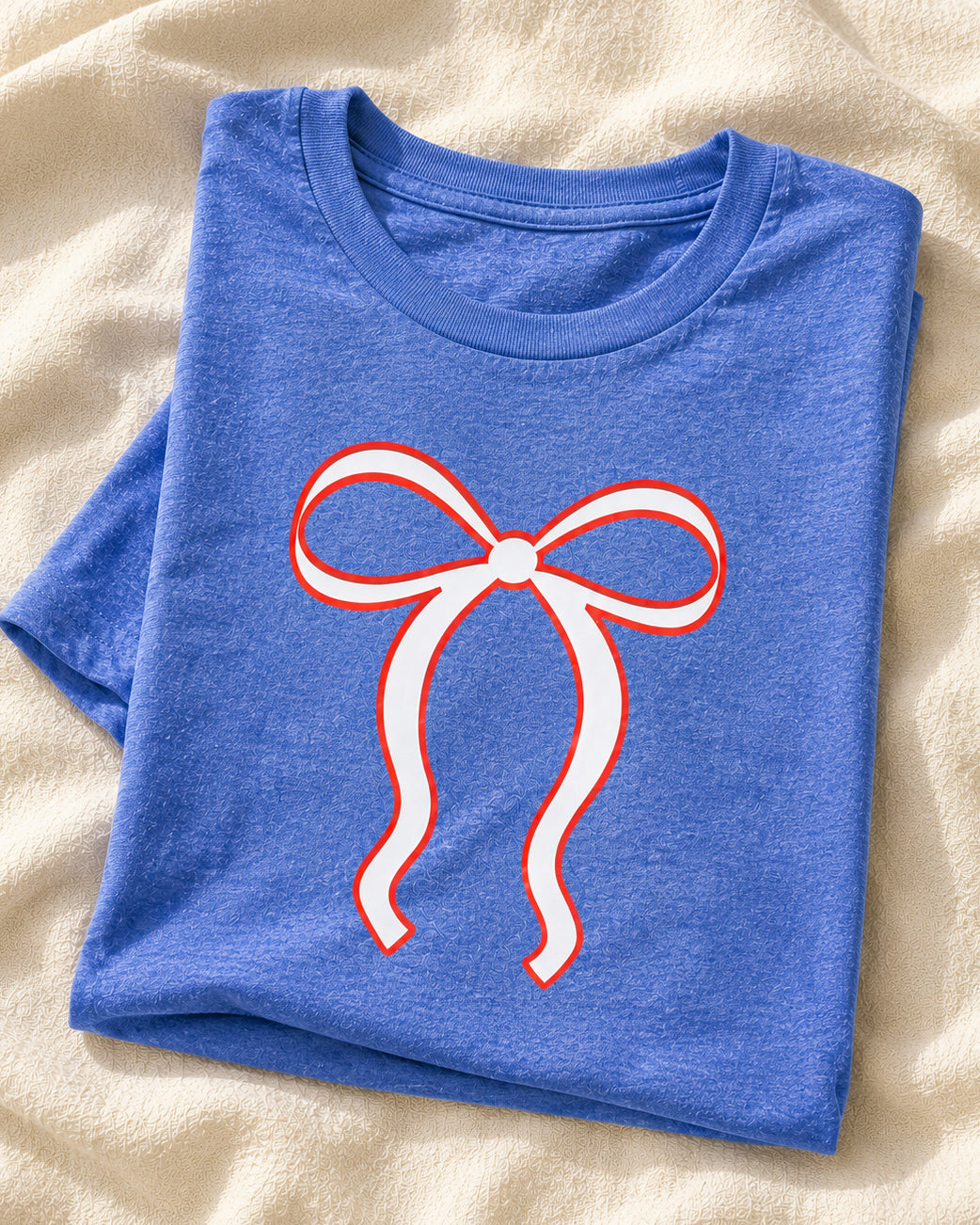 Flat lay of the Liberty Belle Bow Tee in heather royal blue featuring a white bow graphic outlined in red.