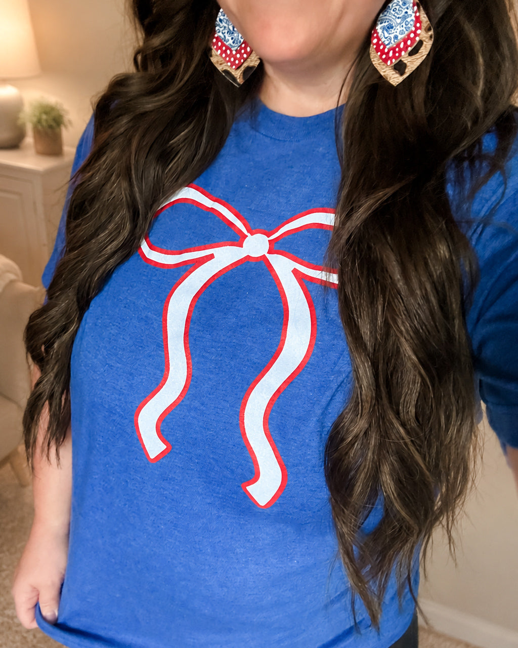 Close-up of the Liberty Belle Bow Tee paired with American Honey Earrings, showing the patriotic bow graphic and relaxed fit.