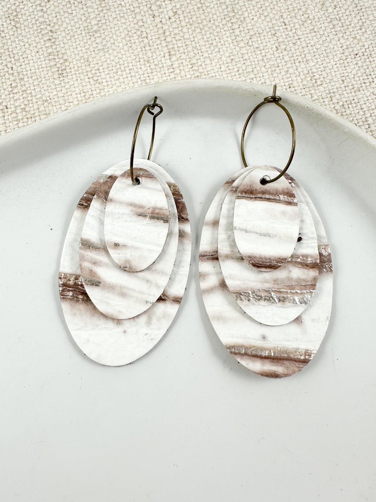 Layered oval leather drop earrings in ivory and neutral tones on a gold hoop.