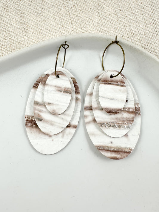 Layered oval leather drop earrings in ivory and neutral tones on a gold hoop.
