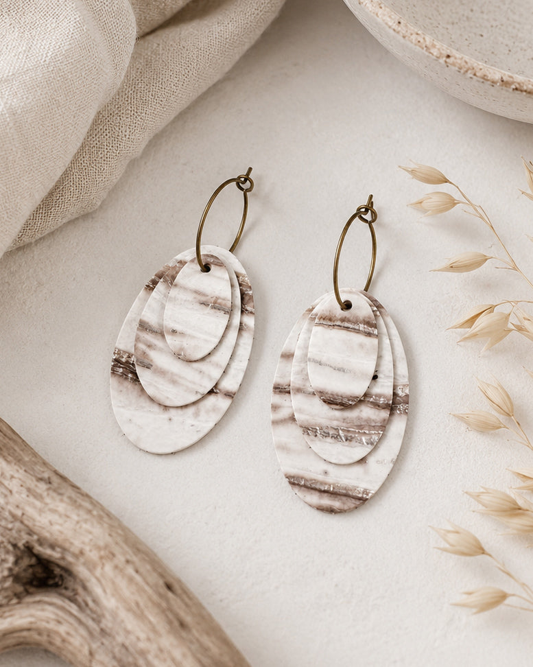 Close-up of Linen Tide Earrings showing the ivory, taupe and warm brown marbled leather layers with neutral natural textures.