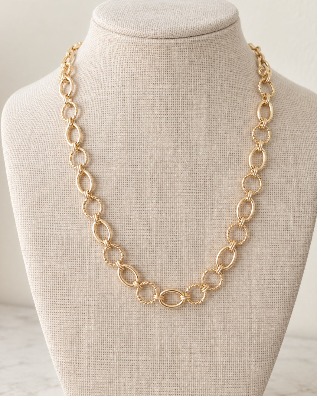 Linked & Lovely gold link necklace displayed on an ivory jewelry bust, featuring alternating smooth oval links and textured round links.