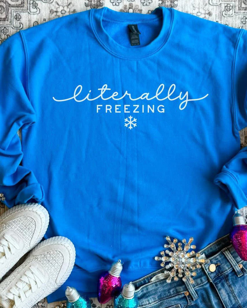 Glacier blue crewneck sweatshirt with white “Literally Freezing” lettering, styled flat lay with jeans and white sneakers.