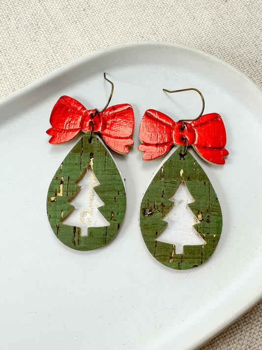 Pair of green cork teardrop earrings with red embossed bows and gold distressing on a white dish