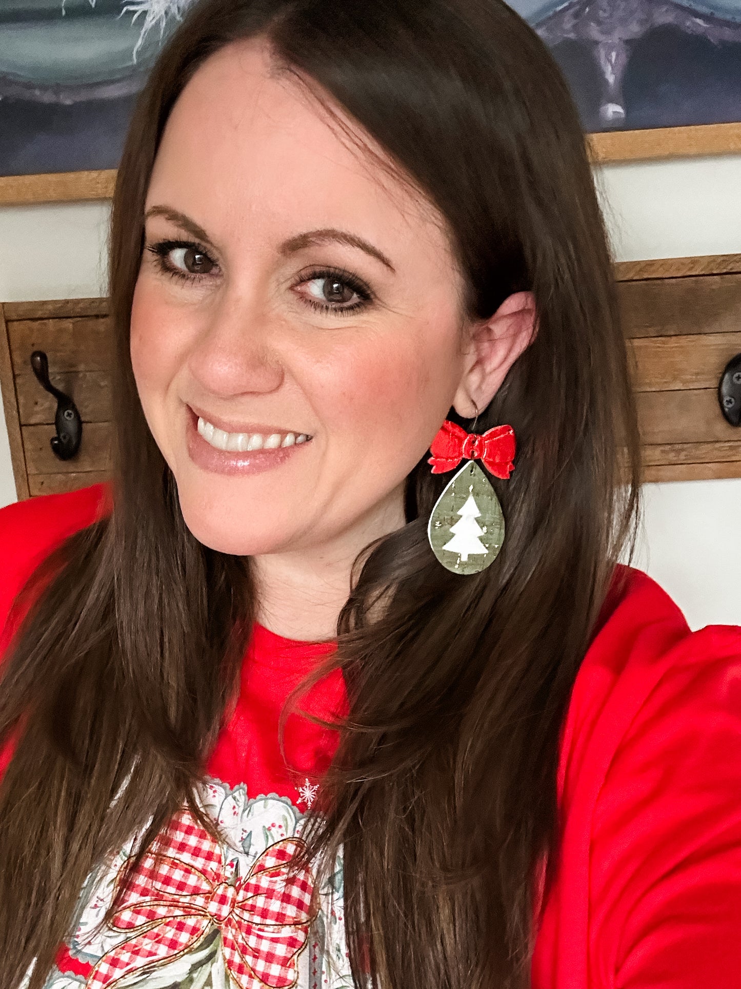Woman wearing green and red holiday earrings with a bow top and cutout tree design