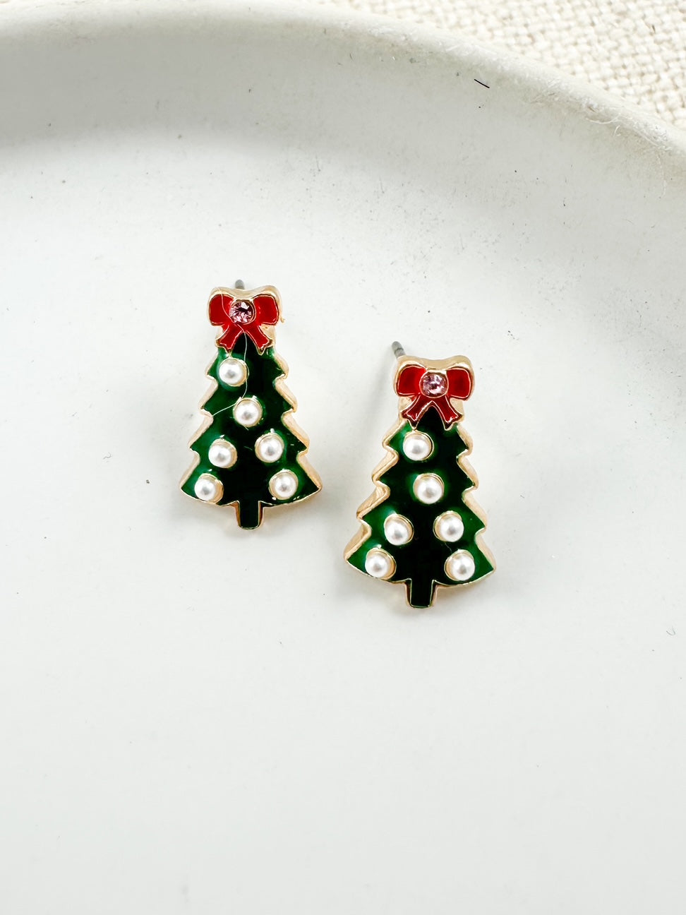 Small green Christmas tree stud earrings with gold trim, pearl accents, and a red bow on top displayed on a light background