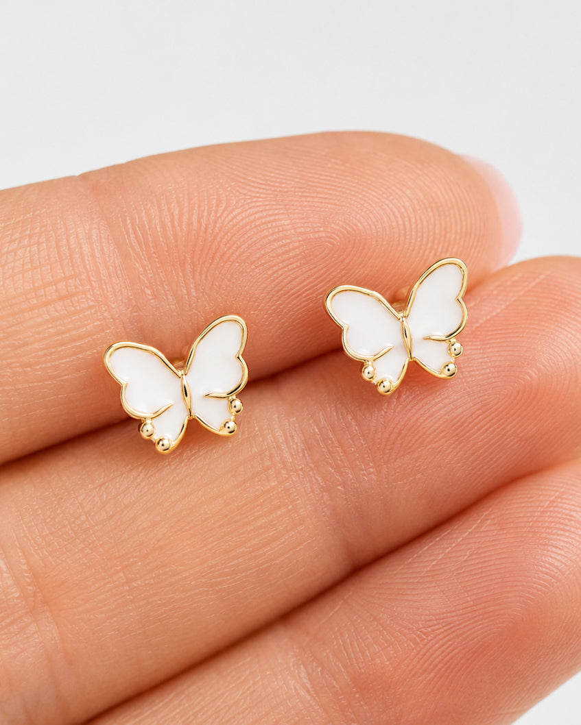 Small white and gold butterfly stud earrings shown in hand to demonstrate their petite size.