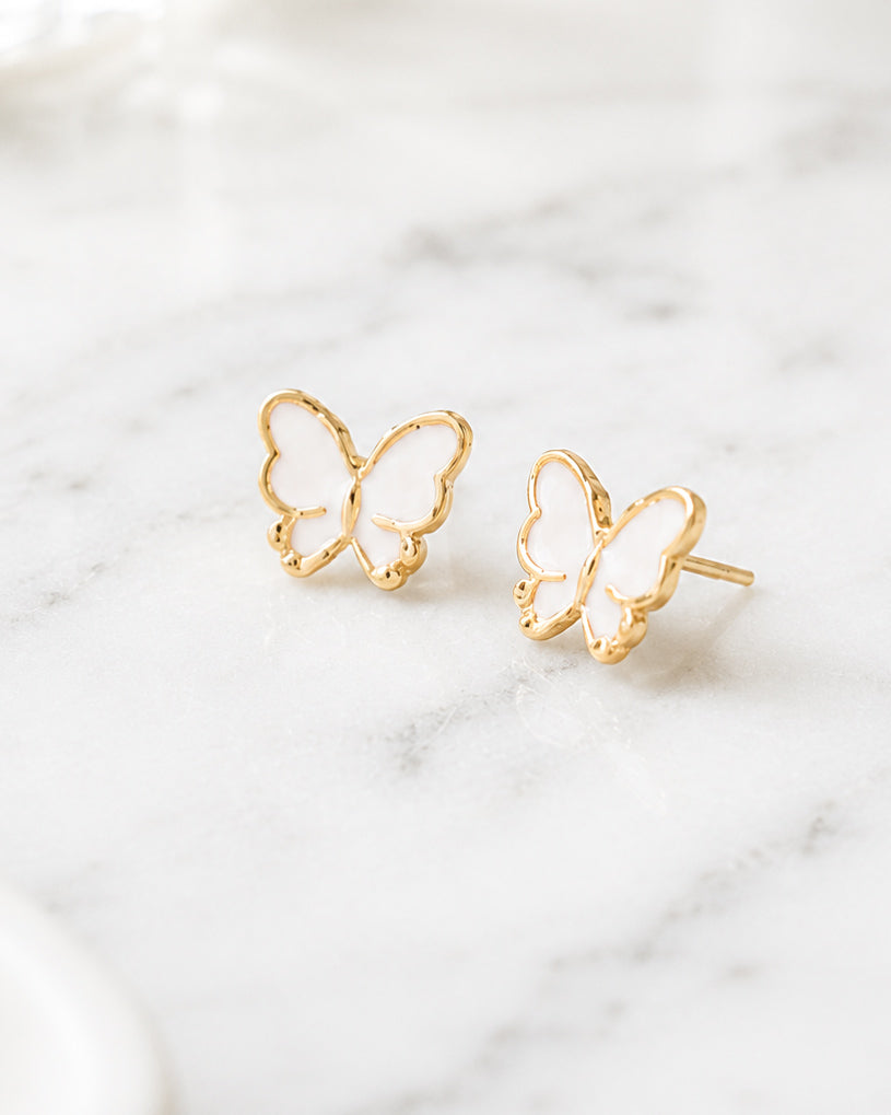 White butterfly stud earrings with gold-tone details displayed on a white marble surface.
