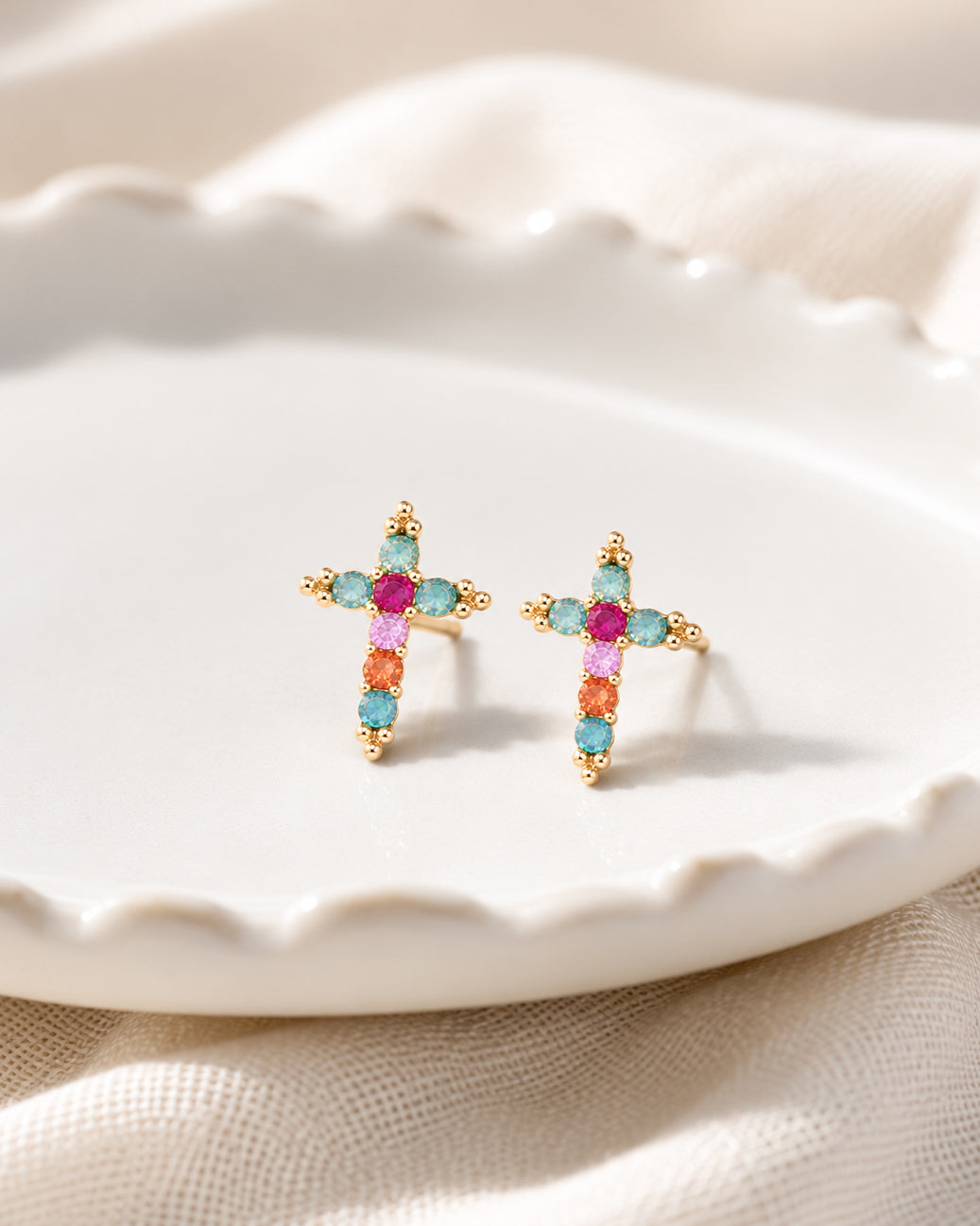 Morning Joy cross stud earrings with colorful faceted stones and gold-tone details displayed in a white jewelry dish