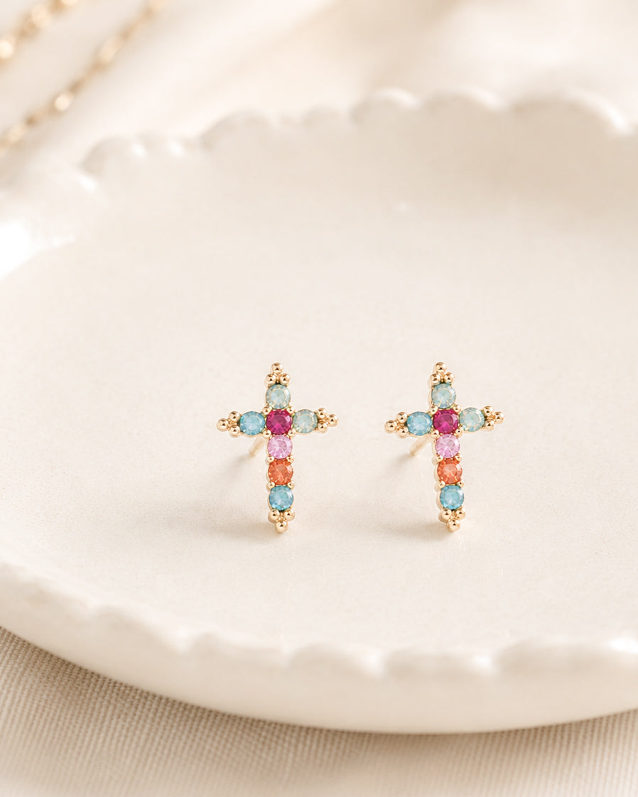 Gold-tone cross stud earrings with colorful faceted stones displayed in a white ceramic jewelry dish