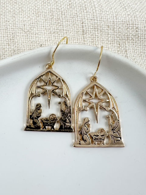 Gold nativity scene earrings with star detail displayed on a white plate