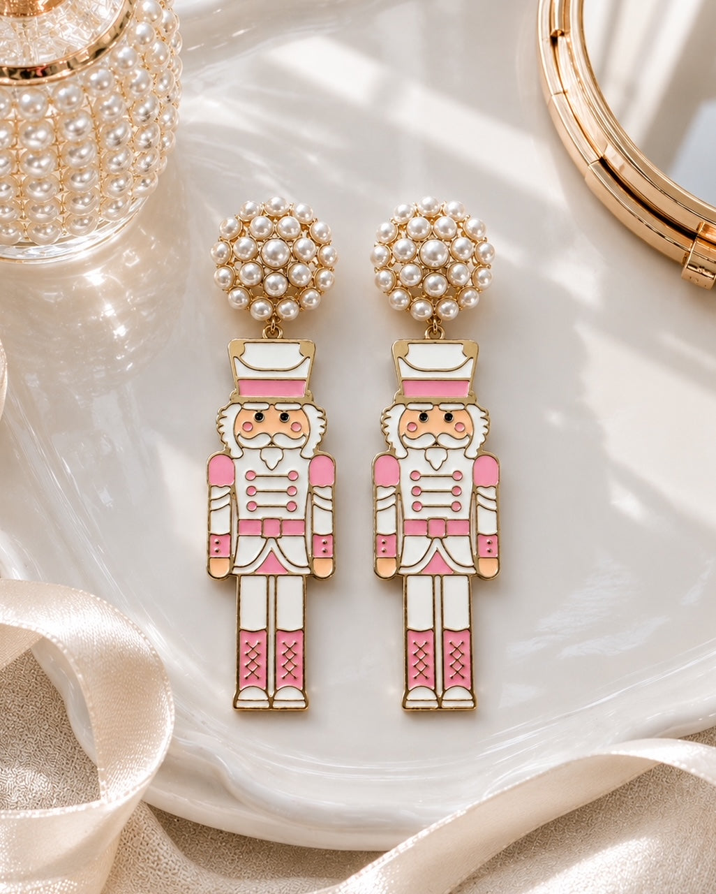 Blush pink nutcracker earrings displayed on a decorative tray with pearl and gold holiday accents.