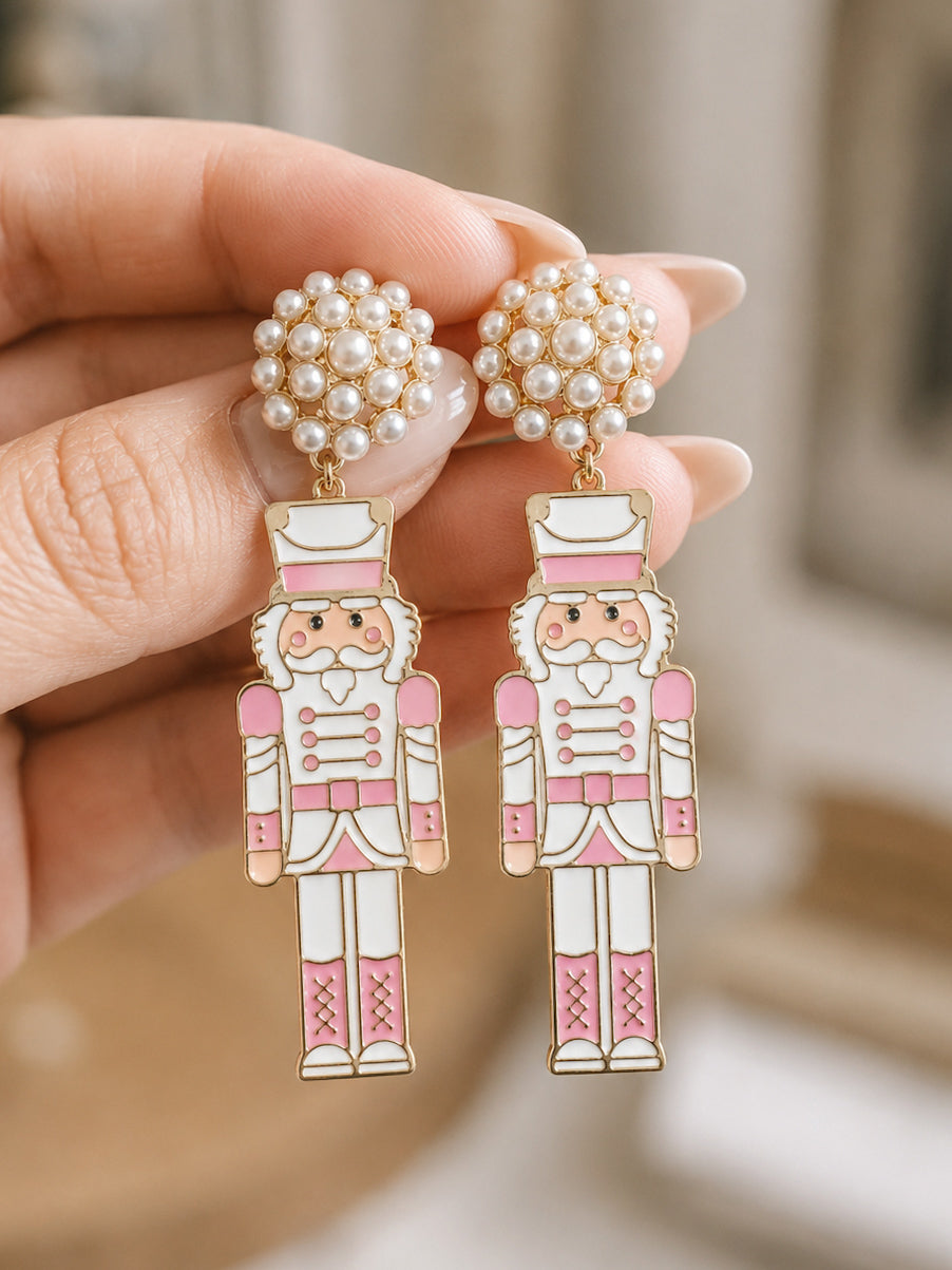 Hand holding blush pink nutcracker earrings with pearl cluster stud tops.