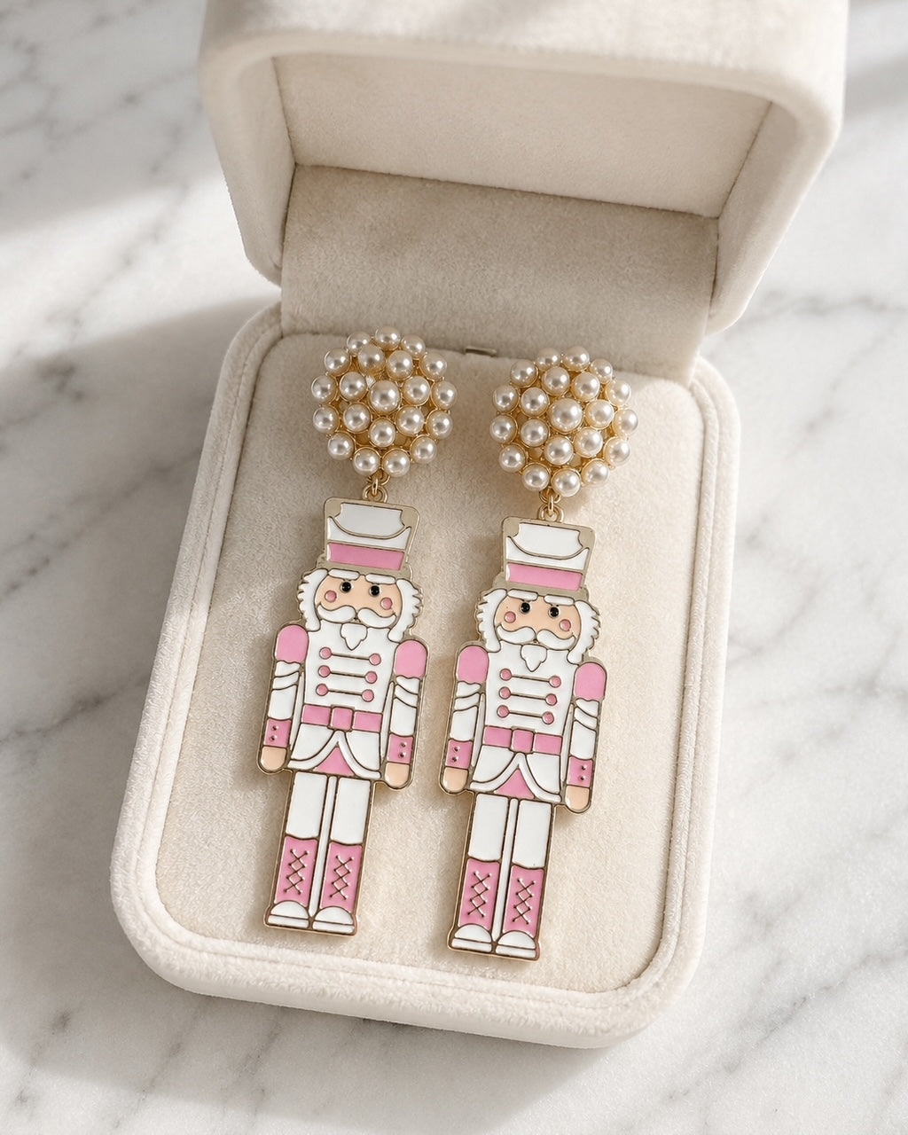 Blush pink nutcracker earrings displayed inside a cream velvet jewelry box.