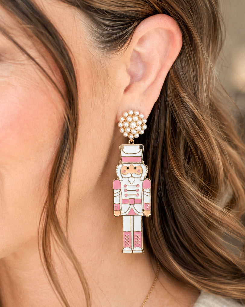 Model wearing blush pink nutcracker statement earrings with pearl cluster studs.