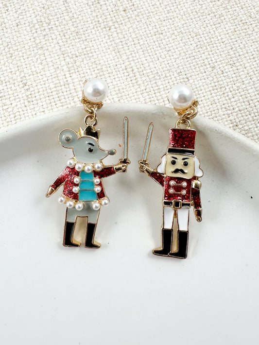 Red Nutcracker and Mouse King earrings with pearl and glitter details displayed on a white dish.
