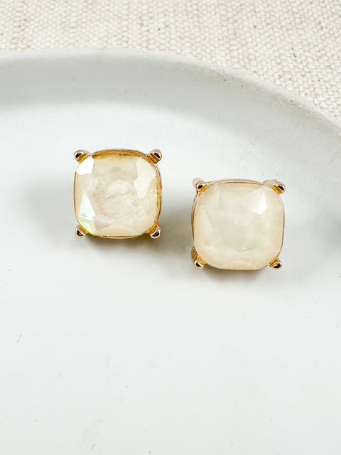 Ivory opal-look square stud earrings with gold hardware on a white ceramic plate