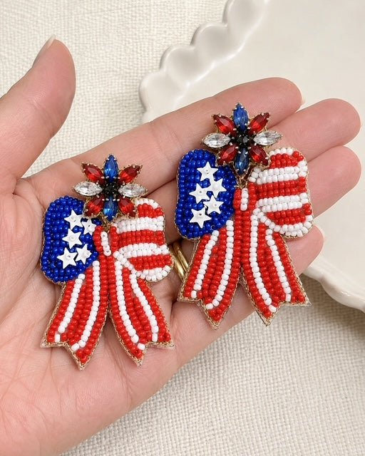 Patriotic Bow Earrings resting in an open hand to show the approximately 2.25-inch size and intricate seed bead details.