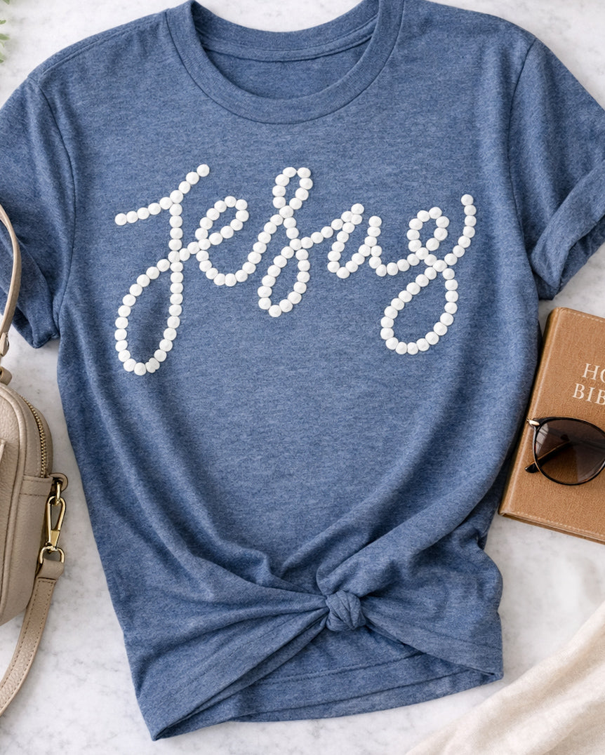 Heather navy graphic t shirt with white pearl style Jesus lettering styled flatlay with bag sunglasses and Bible