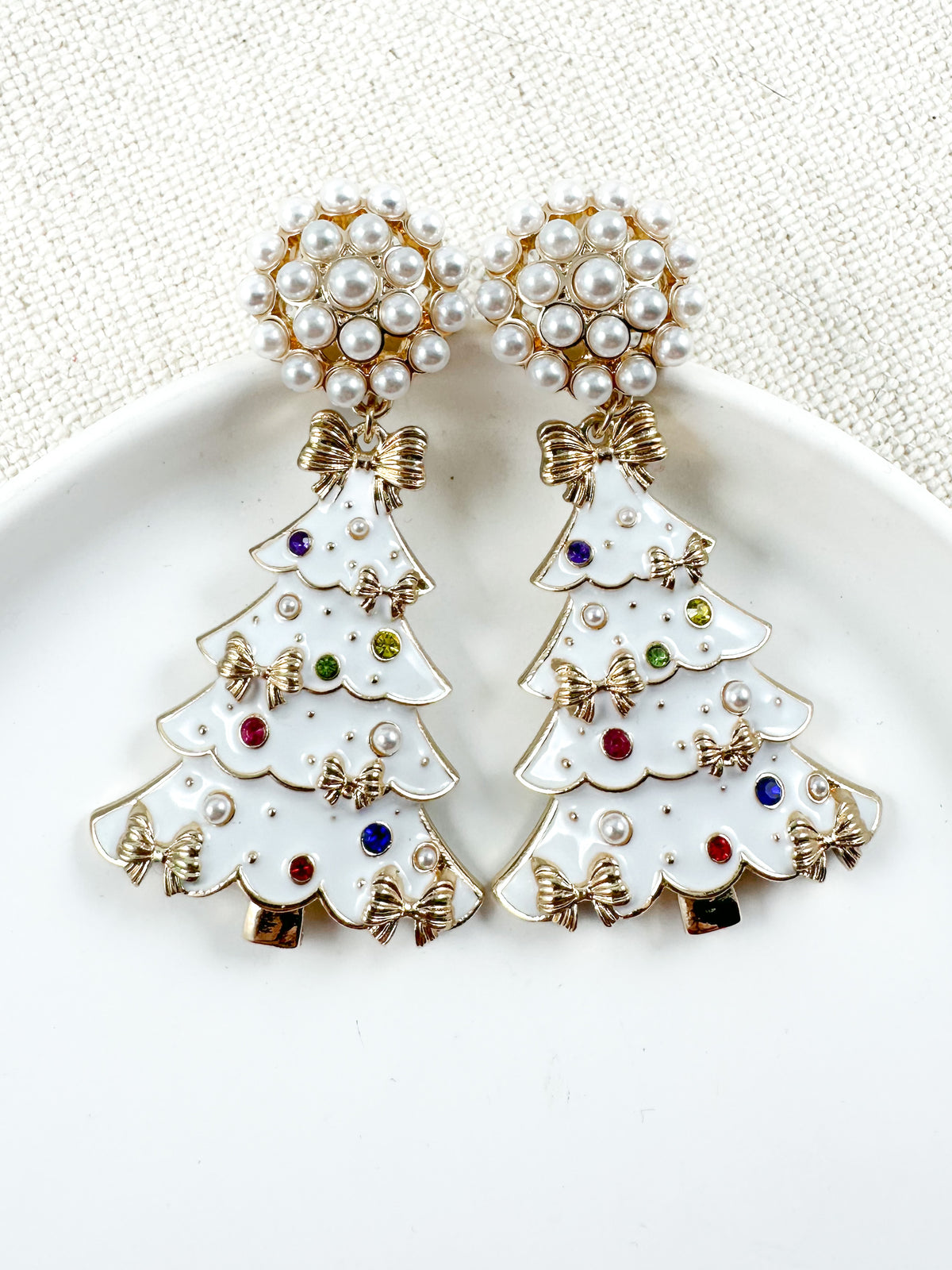 White Christmas tree earrings with pearl cluster stud tops, gold bow accents, and small jeweled details on a white background