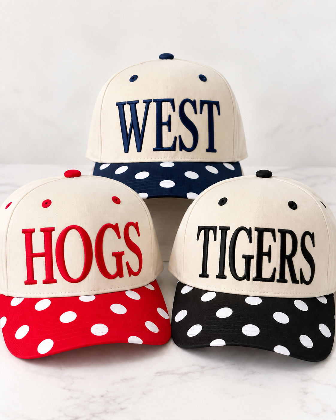 Three customizable Pep Rally Hats with cream crowns and polka dot bills, shown in navy with WEST embroidery, red with HOGS embroidery, and black with TIGERS embroidery.