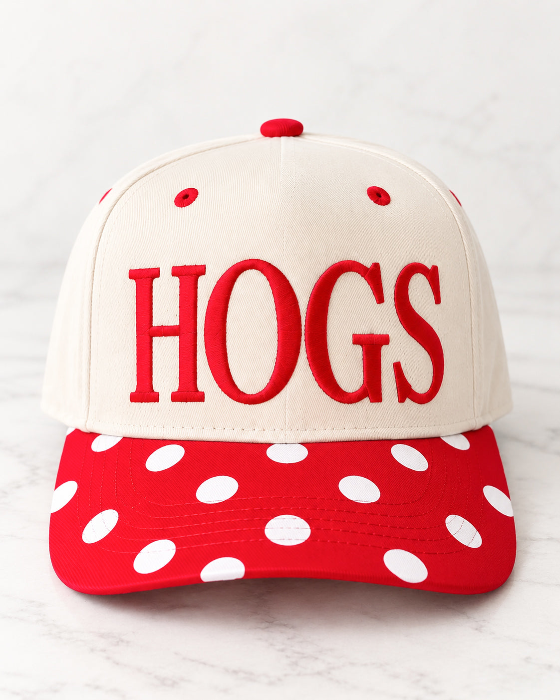 Front view of a cream Pep Rally Hat with red HOGS embroidery, red eyelets, and a red curved bill with white polka dots.