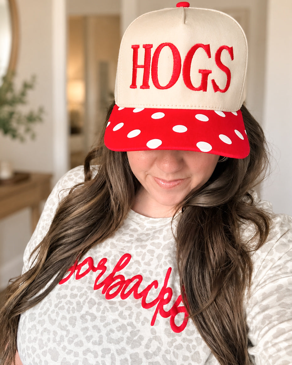 Woman wearing a cream HOGS hat with red embroidery and a red polka dot bill, paired with a light leopard print Arkansas graphic tee.