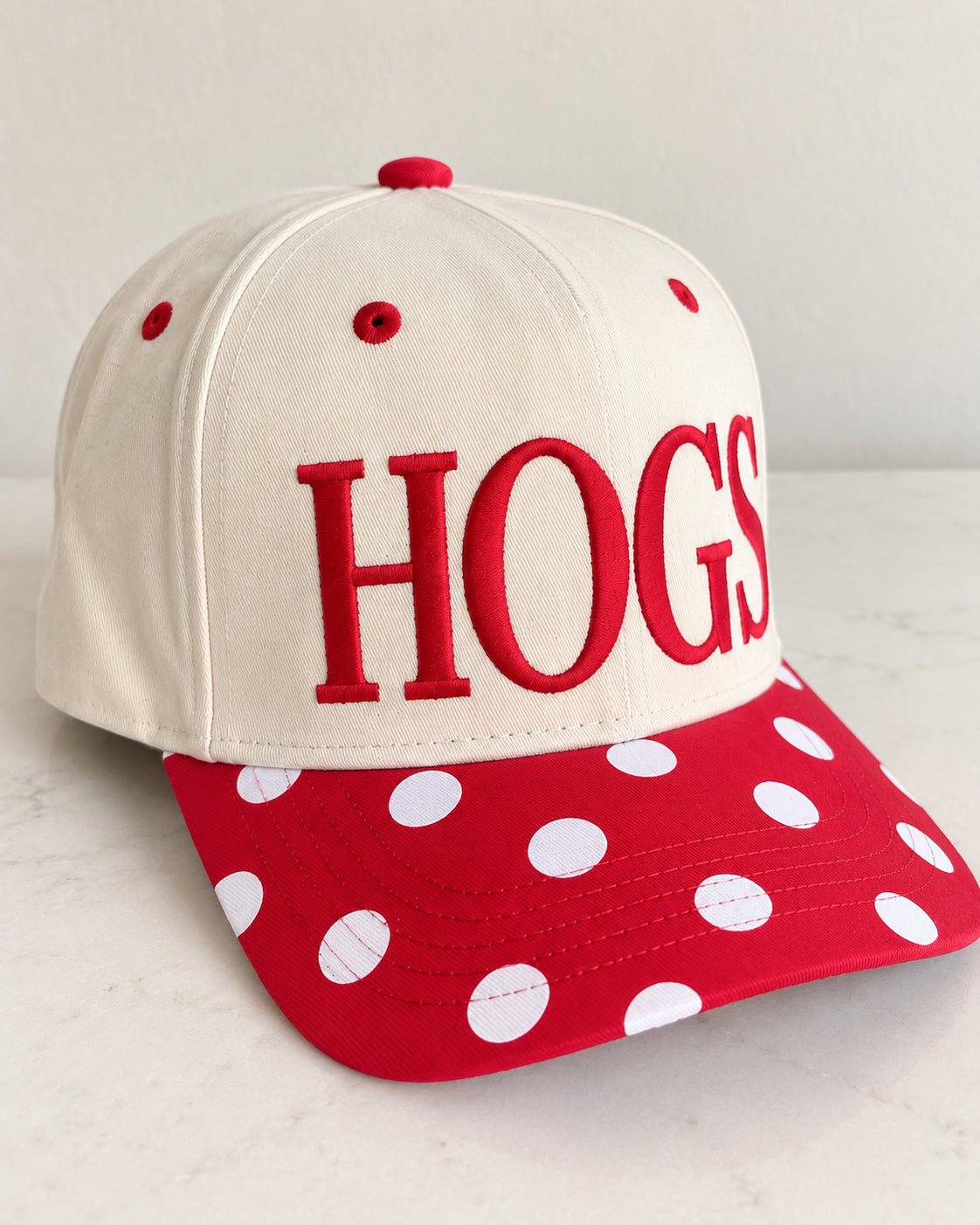 Angled view of the cream and red Pep Rally Hat showing the embroidered HOGS lettering, structured crown, and curved polka dot bill.